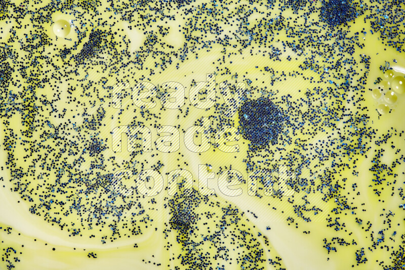 A close-up of sparkling blue glitter scattered on swirling yellow background