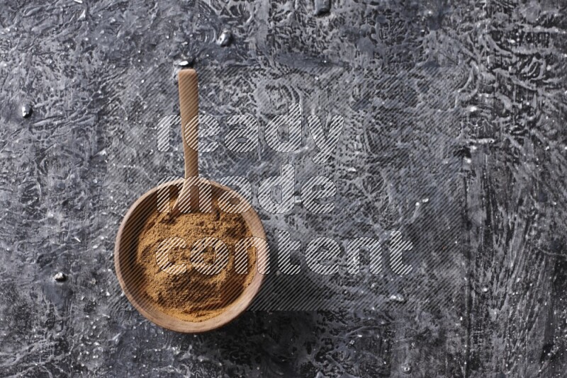 Wooden bowl full of cinnamon powder with a wooden spoon on a textured black background in different angles
