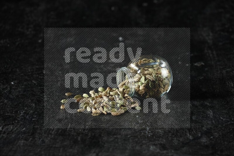 وعاء زجاجي للتوابل مقلوب ممتلئ بحبوب الهيل على خلفية سوداء