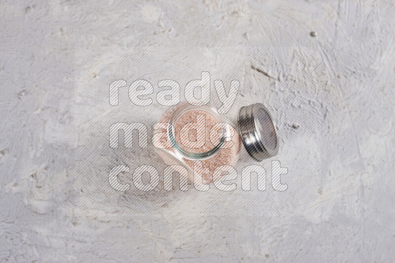 A glass jar full of fine himalayan salt on white background