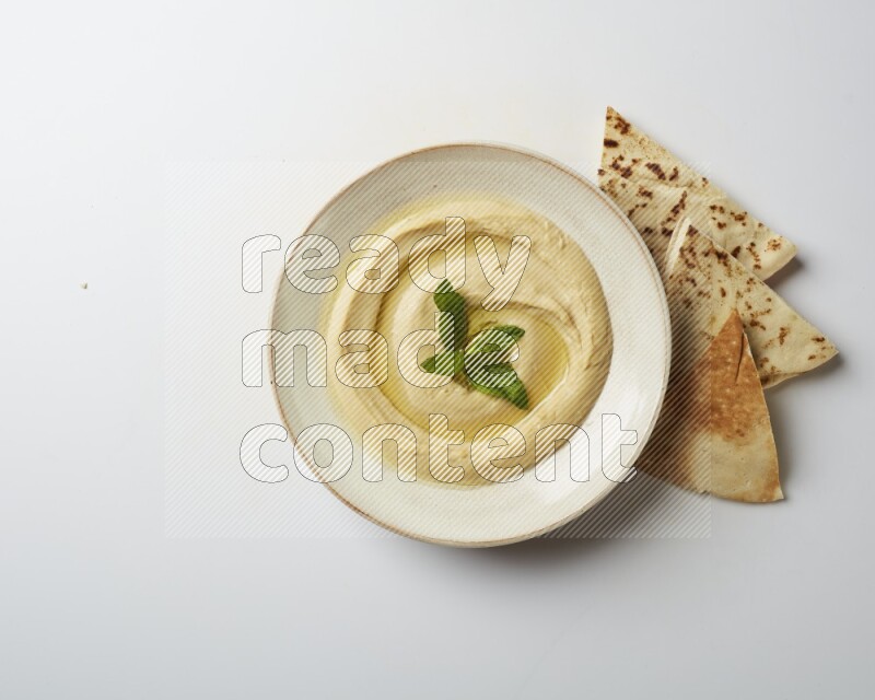 Hummus in a pottry plate garnished with mint  on a white background