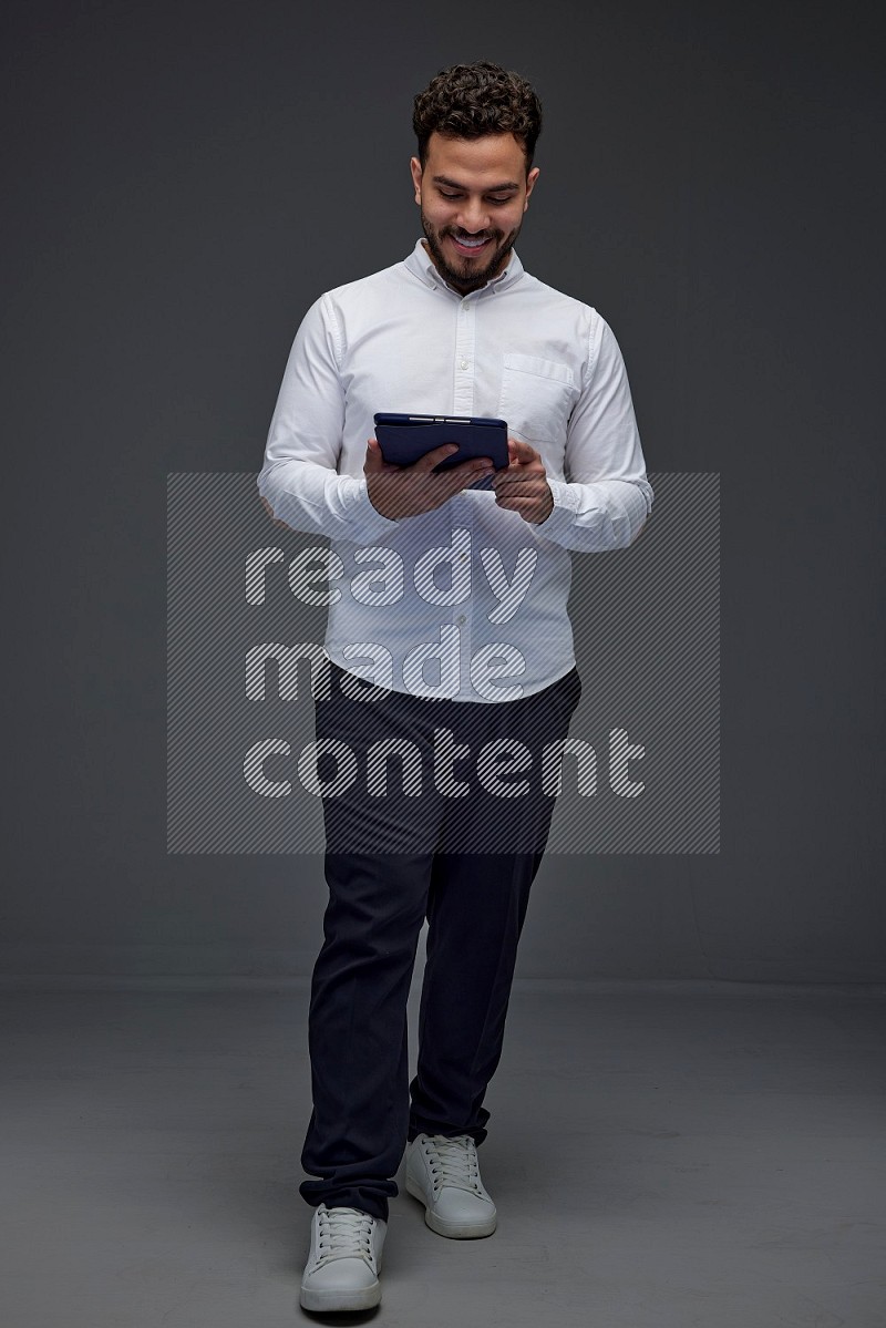 A man wearing smart casual standing and using his tablet eye level on a gray background
