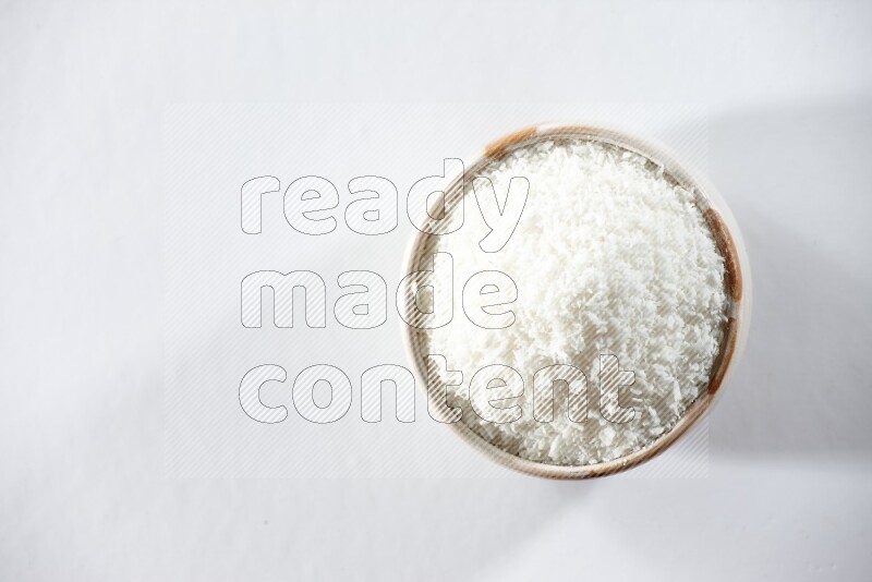 A beige ceramic bowl full of desiccated coconut on a white background in different angles