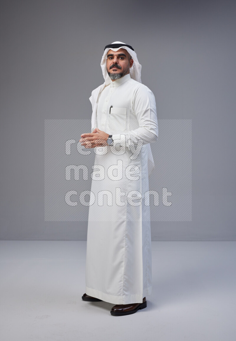 Saudi man Wearing Thob and white Shomag standing interacting with the camera on Gray background