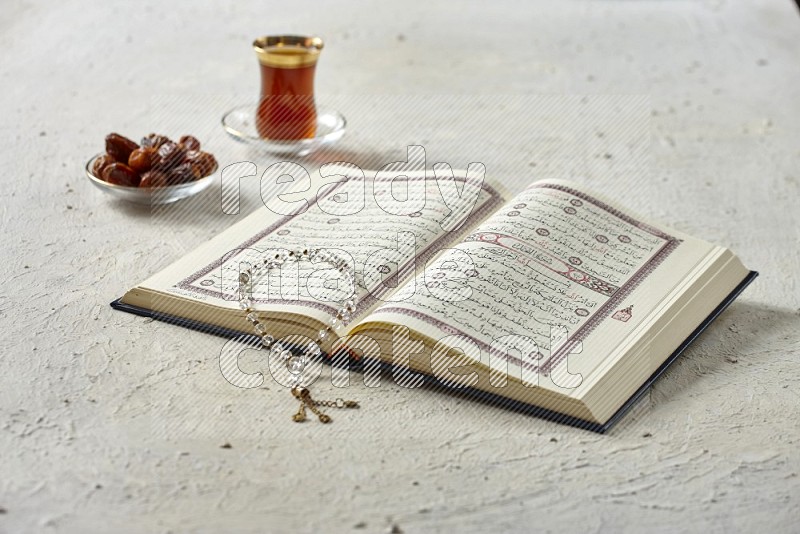 Quran with dates, prayer beads and different drinks all placed on textured white background