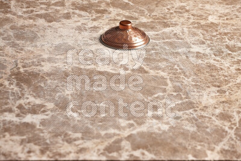 A small copper pot lid on beige marble background