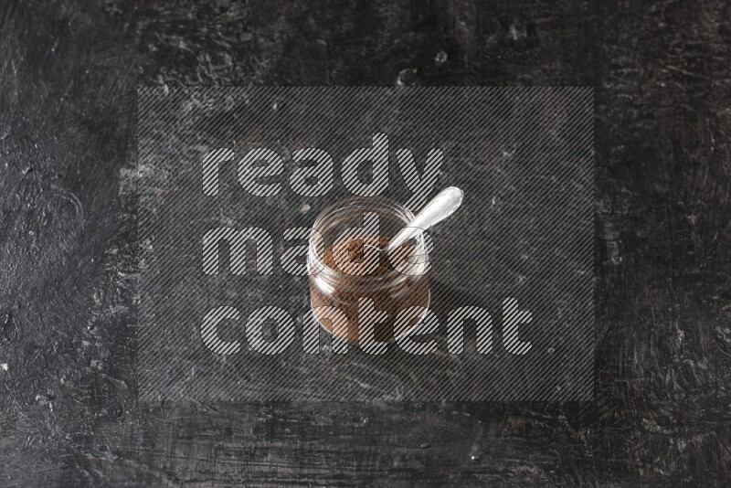 وعاء زجاجي ممتلئ ببودرة القرنفل مع ملعقة معدنية على أرضية سوداء