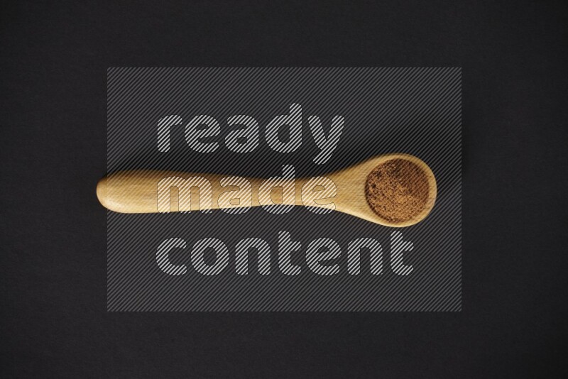 Cinnamon powder in a wooden spoon on a black background