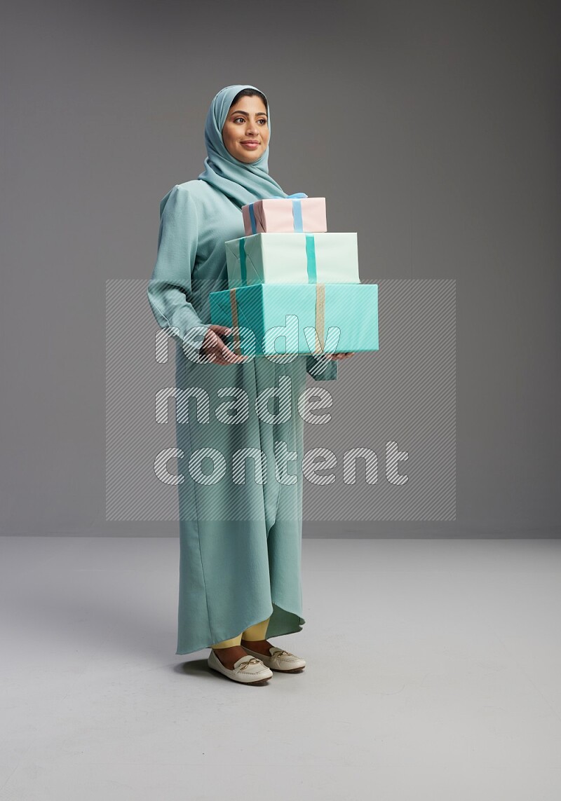 Saudi Woman wearing Abaya standing holding gift box on Gray background