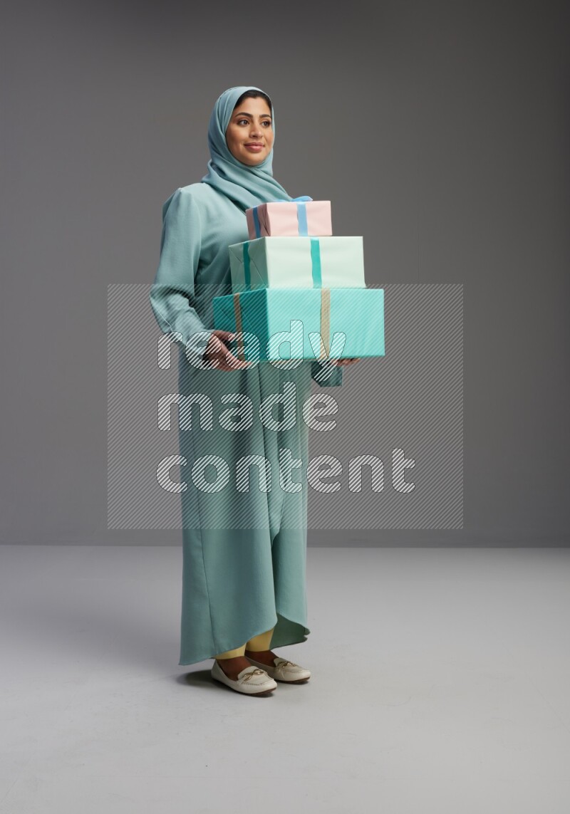 Saudi Woman wearing Abaya standing holding gift box on Gray background