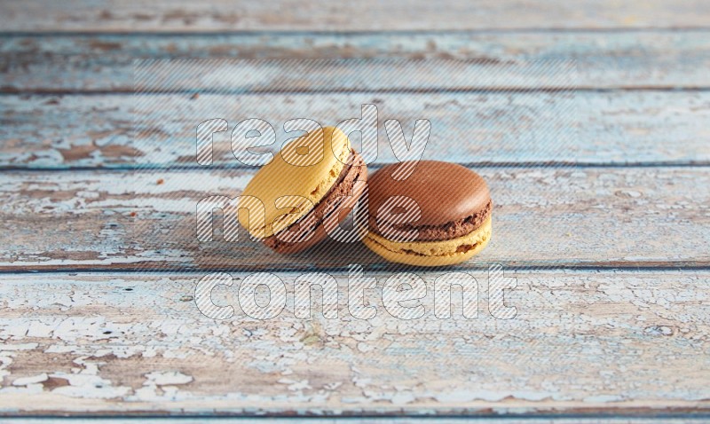 45º Shot of two Yellow and Brown Chai Latte macarons on light blue wooden background