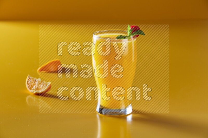 glass of orange juice with berry & mint on yellow background