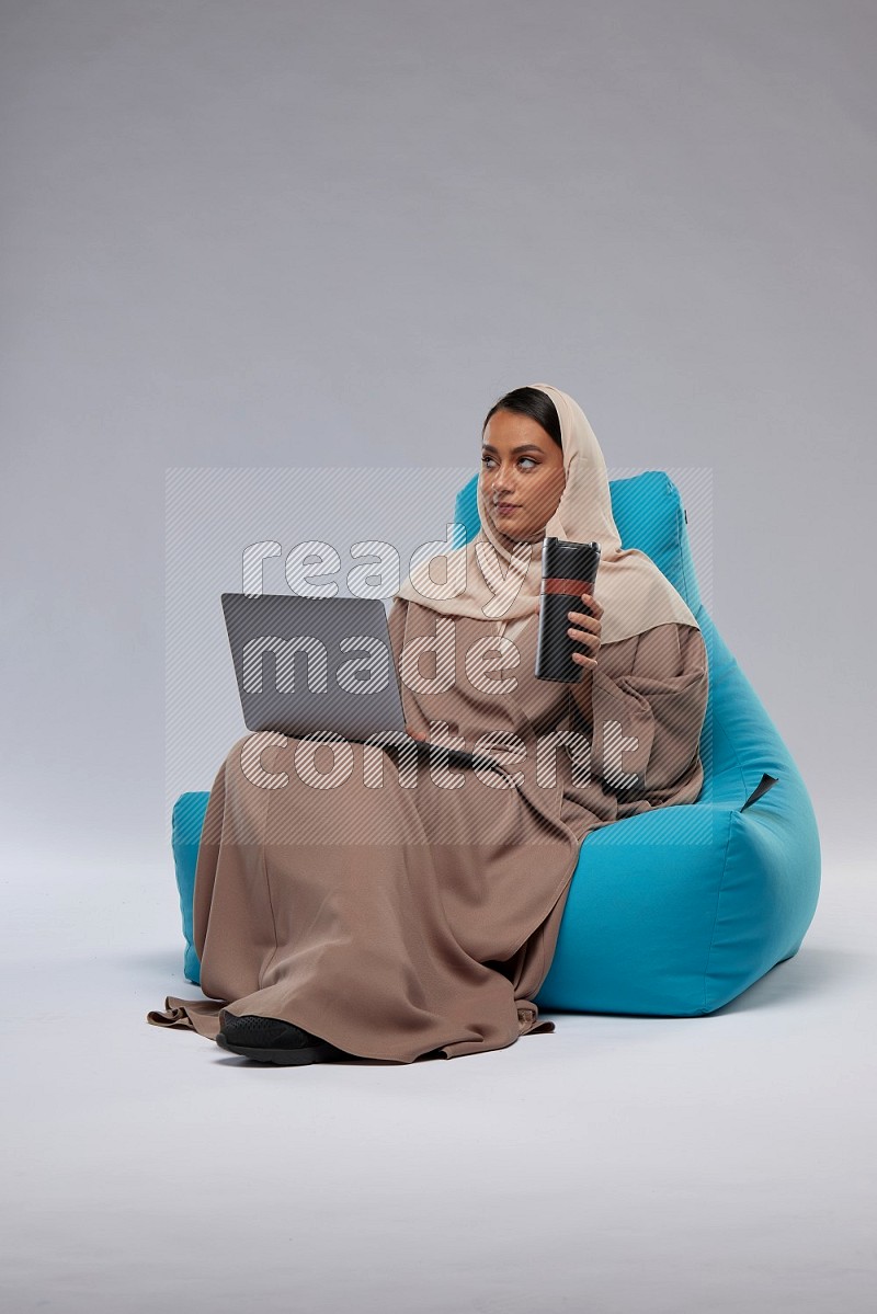 A Saudi woman sitting on a blue beanbag and working on laptop