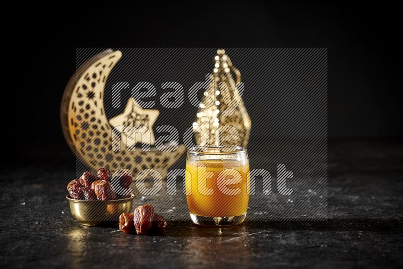 تمر في وعاء معدني مع مشروب قمر الدين بجانب فوانيس ذهبية علي خلفية سوداء