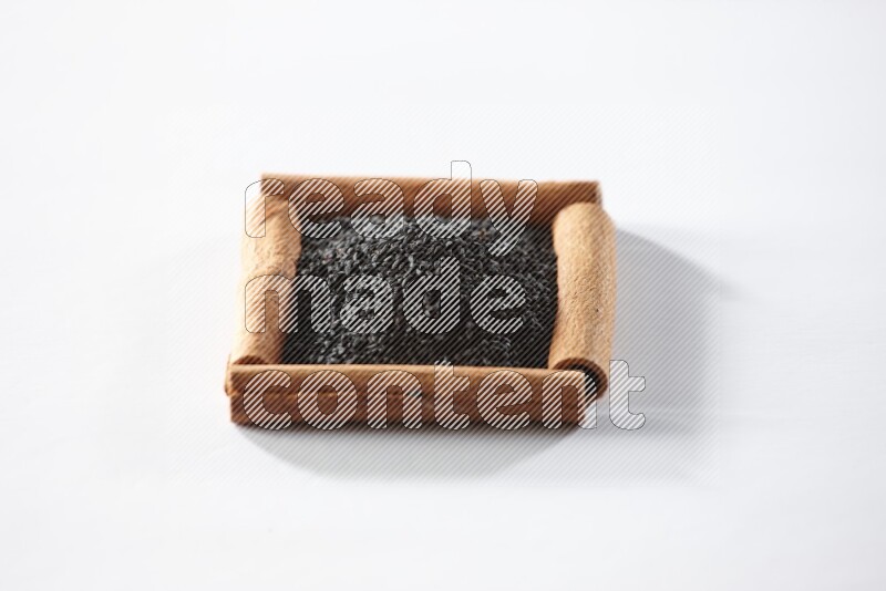 أربعة من أعواد القرفة مكونة شكل مربع بداخلها حبة البركة علي خلفية بيضاء