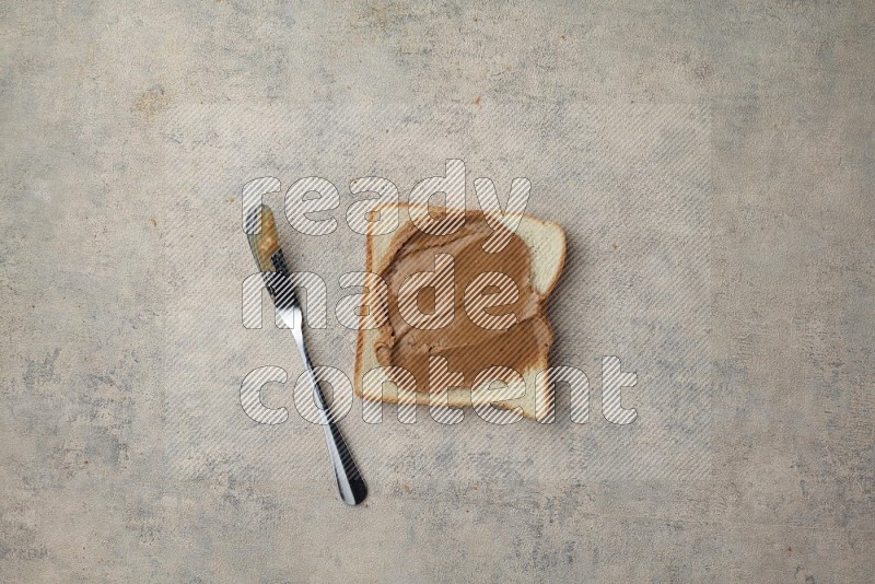 creamy peanut butter on a white toast with a spreading knife on a light blue textured background