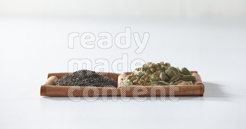 مربعان من أعواد القرفة ممتلئان بالشاي الأسود وحبوب الهال علي خلفية بيضاء