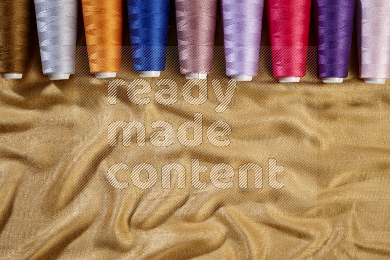 Multicolored sewing thread spools on yellow fabric background