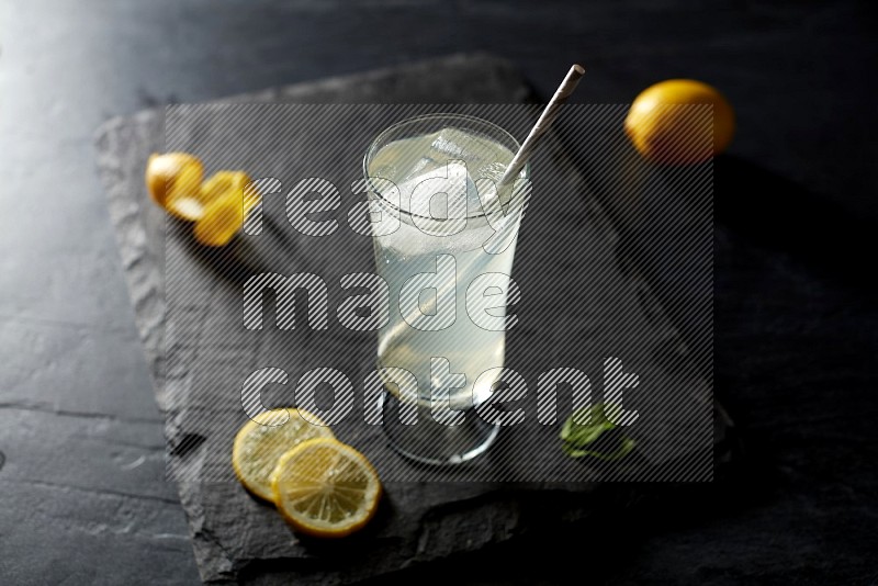 A glass of lemon juice with a straw on black background