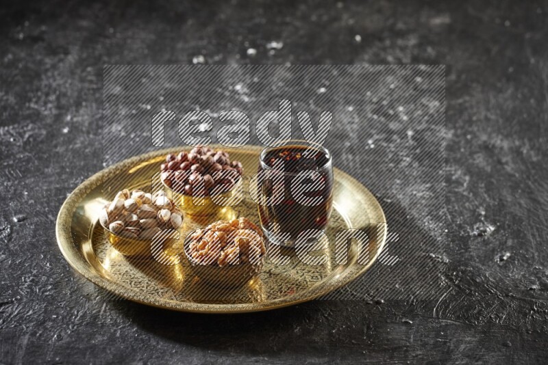 مكسرات في أطباق معدنية مع مشروب التمر الهندي على صينية علي خلفية سوداء