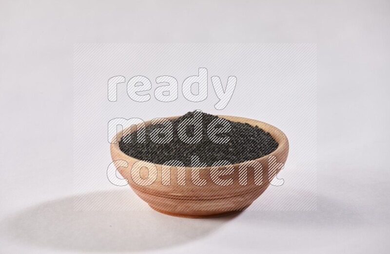 A wooden bowl full of black seeds on a white flooring