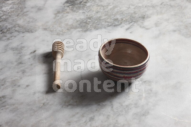 Multicolored pottery bowl with wooden honey dipper on the side on grey marble background
