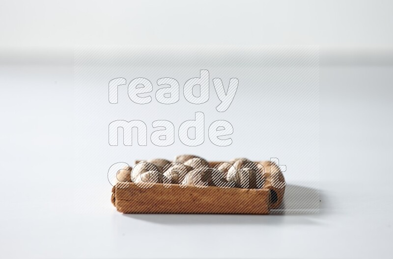 أربعة من أعواد القرفة مكونة شكل مربع بداخلها جوزة الطيب علي خلفية بيضاء