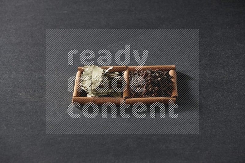 مربعان من أعواد القرفة ممتلئان بالقرنفل وأوراق الغار علي خلفية سوداء