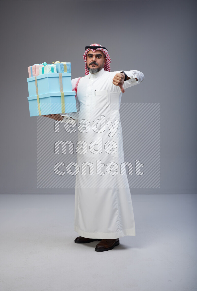 Saudi man Wearing Thob and red Shomag standing holding gift box on Gray background