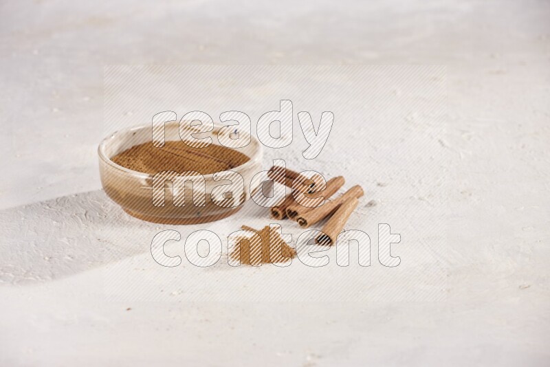Ceramic bowl full of cinnamon powder with cinnamon sticks on the side on white background