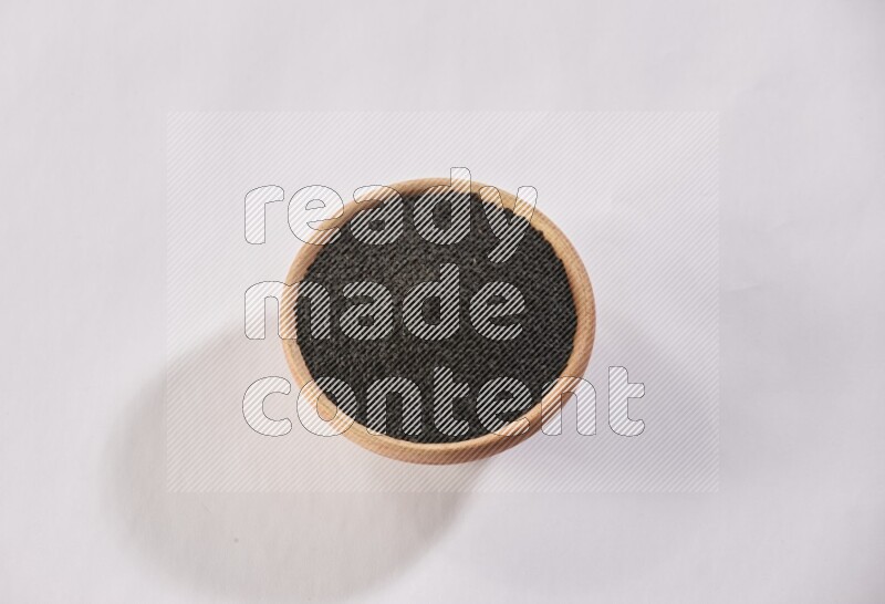A wooden bowl full of black seeds on a white flooring