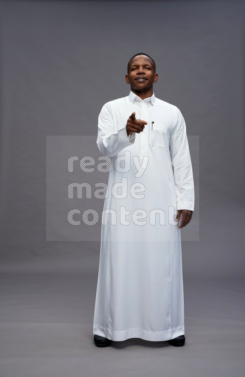 Saudi man wearing thob standing interacting with the camera on gray background