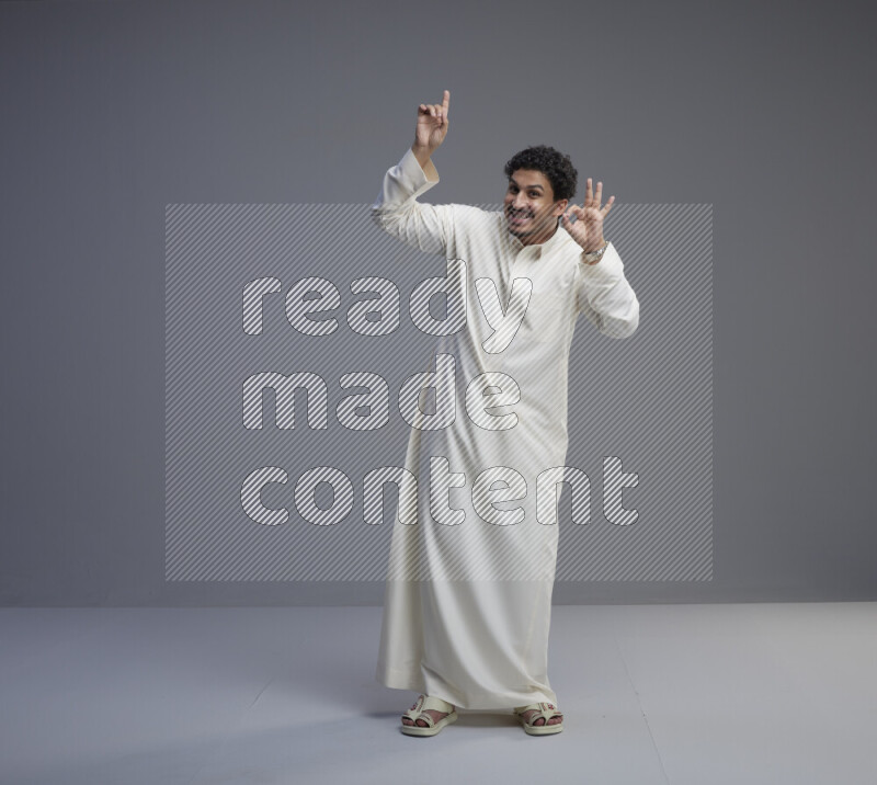 A Saudi man standing wearing thob interacting with the camera on gray background