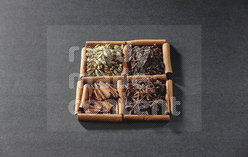 4 squares of cinnamon sticks full of cinnamon, cardamom, cloves and star anise on black flooring
