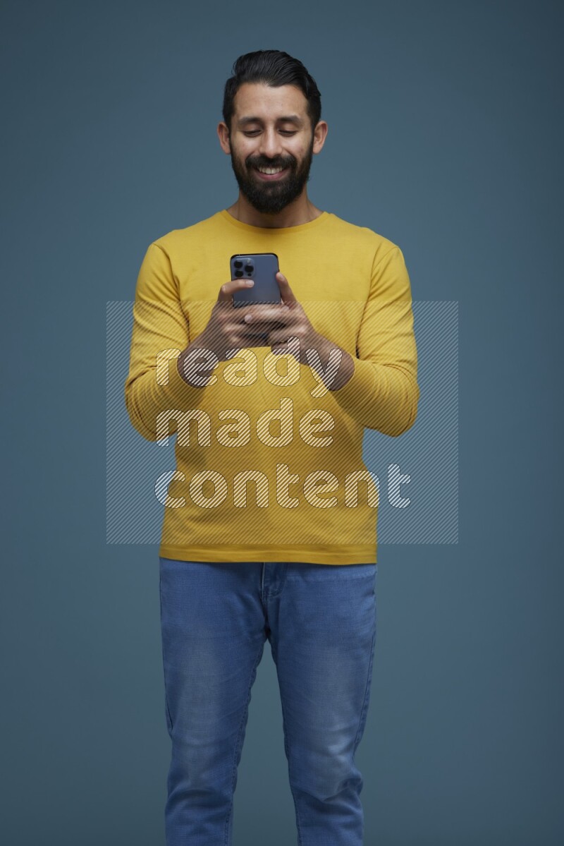 Man typing on his phone in a blue background wearing a yellow shirt