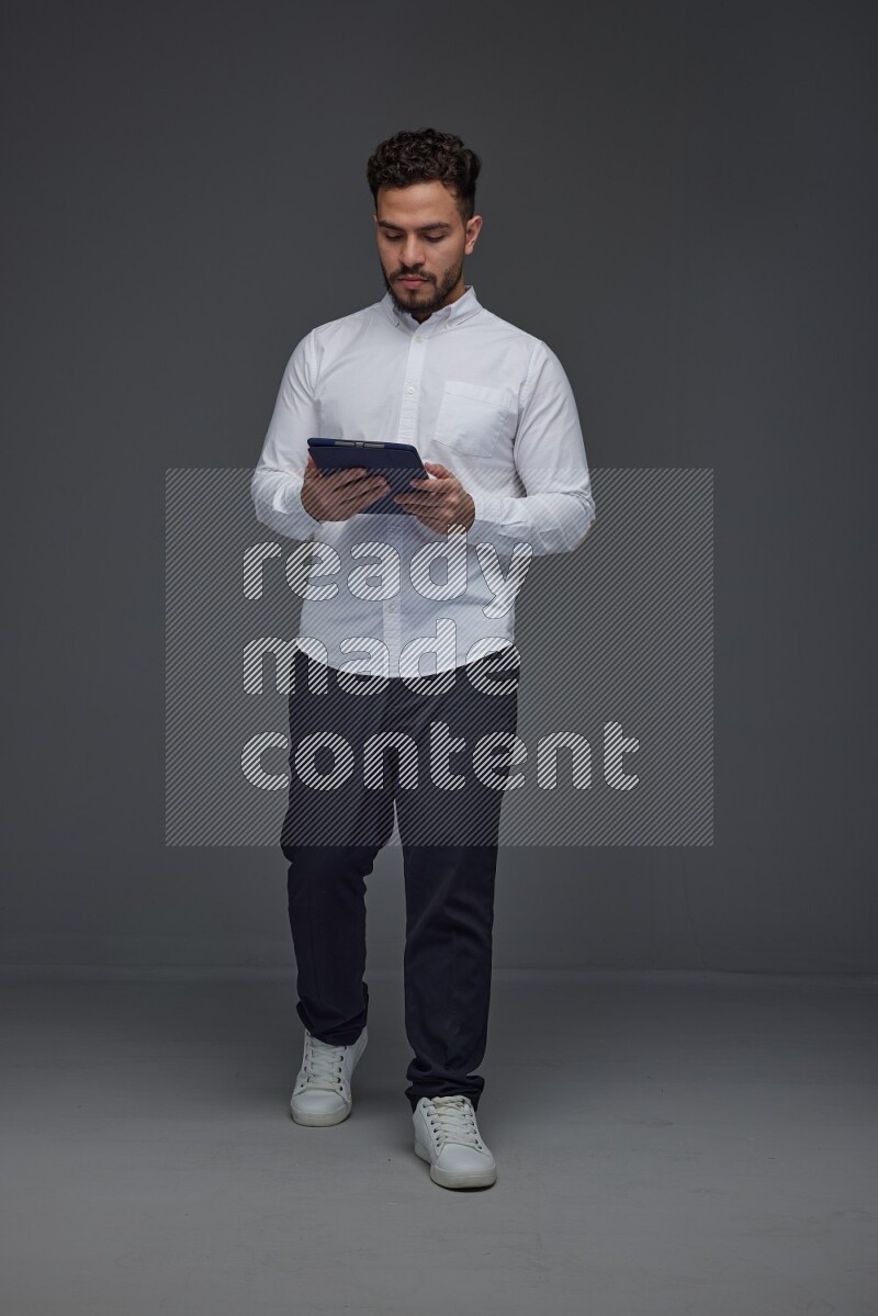 A man wearing smart casual standing and using his tablet eye level on a gray background