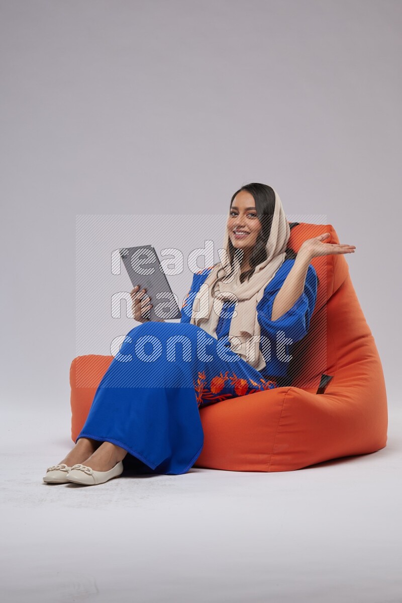 A Saudi woman sitting on an orange beanbag and working on tablet