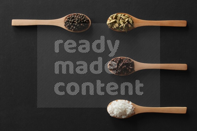 الفلفل الأبيض والقرنفل والهيل والملح والفلفل الأسود وريحان مجفف في معالق خشبية علي خلفية سوداء