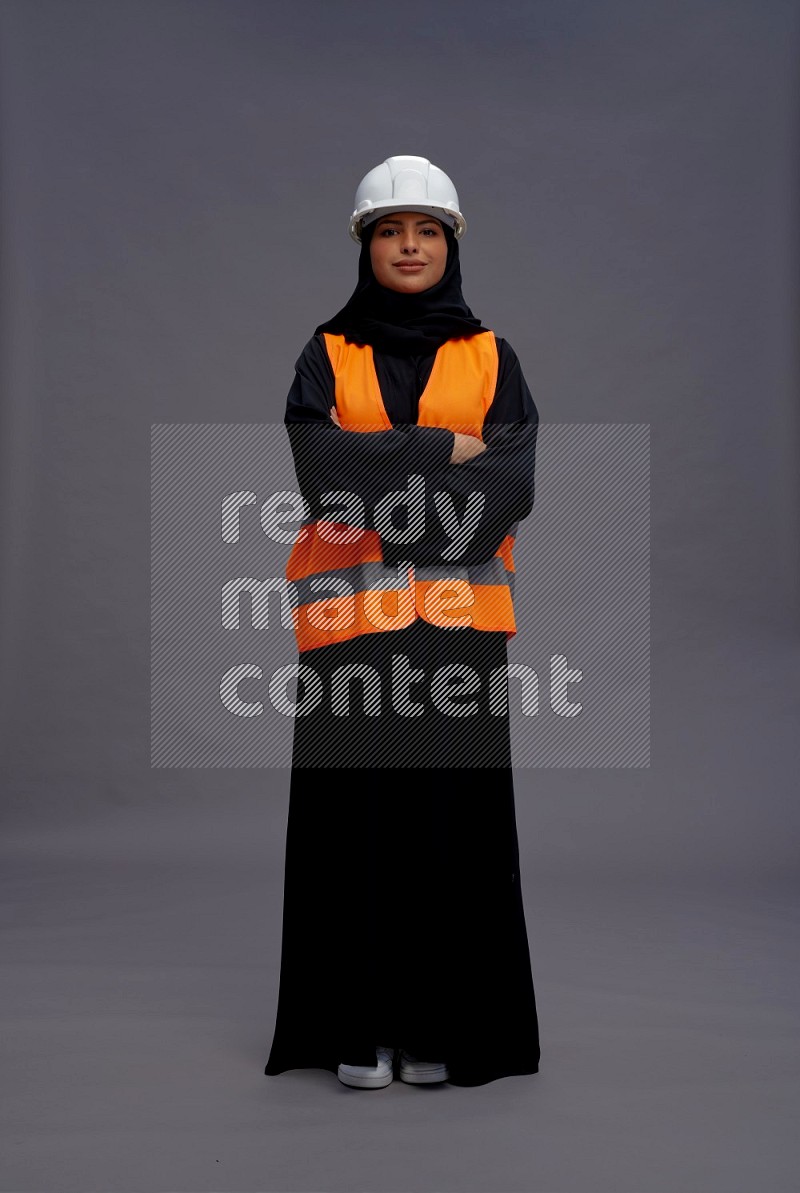 Saudi woman wearing Abaya with engineer vest standing with crossed arms on gray background