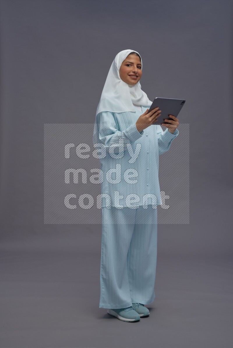 Saudi woman wearing hijab clothes standing working on tablet on gray background