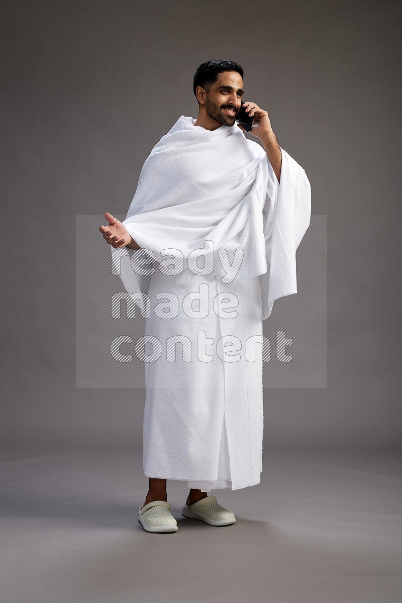 A man wearing Ehram Standing talking on phone on gray background