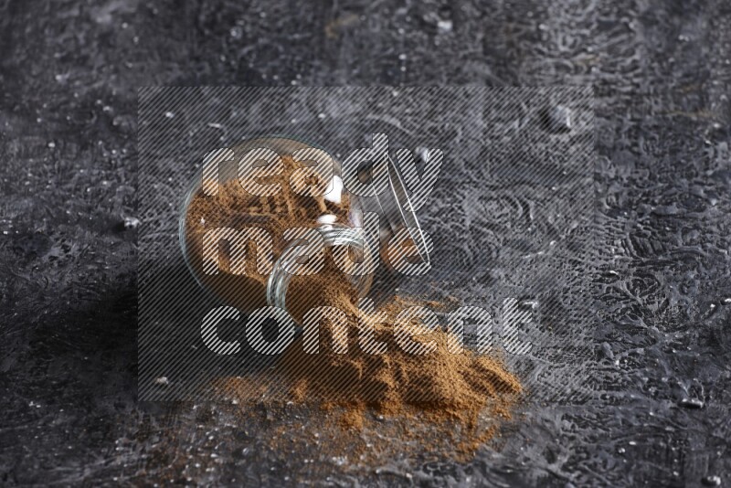 Flipped herbal glass jar full of cinnamon powder on textured black background