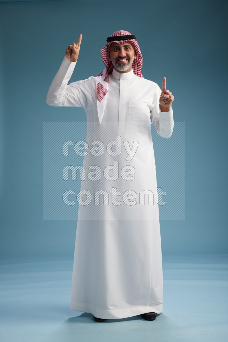 Saudi man wearing thob and shomagh posing to the camera on blue background