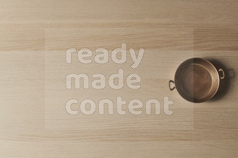 مقلاة نحاسية صغيرة على خلفية خشبية فاتحة