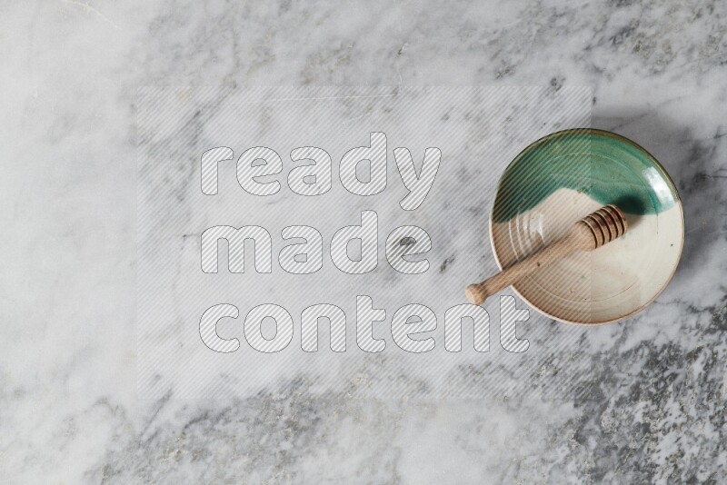Multicolored pottery plate with wooden honey dipper in it on grey marble background