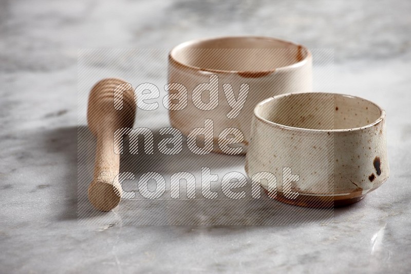 Multicolored Pottery bowls with wooden honey handle on the side with grey marble flooring, 15 degree angle