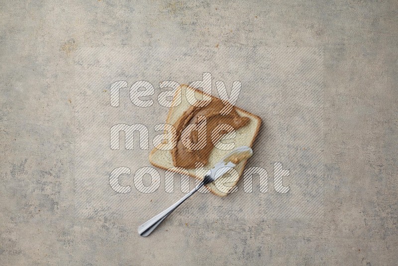 creamy peanut butter on a white toast with a spreading knife on a light blue textured background