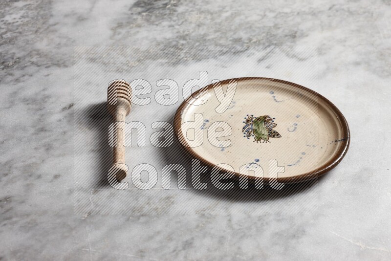 Decorative pottery plate with wooden honey dipper on the side on grey marble background