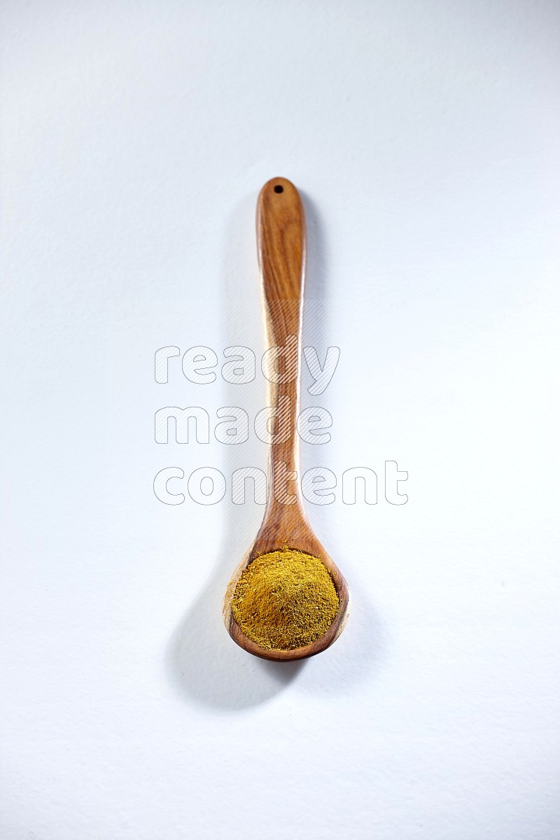A wooden ladle full of turmeric powder on white flooring