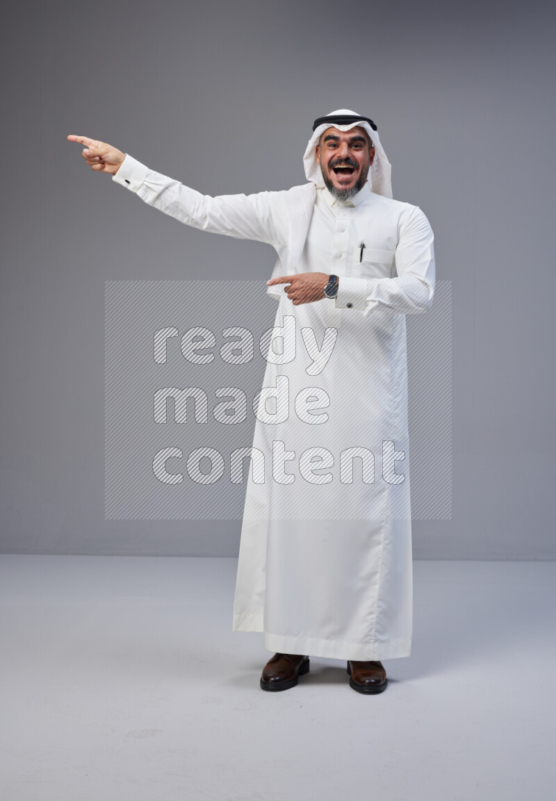 Saudi man Wearing Thob and white Shomag standing interacting with the camera on Gray background
